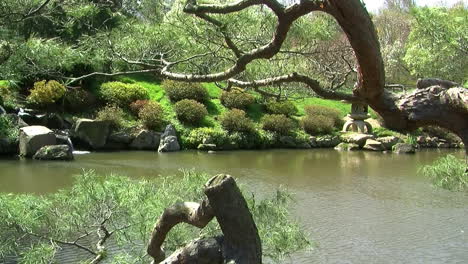 Camera-jibs-from-right-to-left-in-Japanese-garden-with-pond,-stone-lantern-and-waterfall