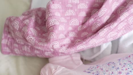 Baby's-hand-is-holding-pink-bed-linen-close-up