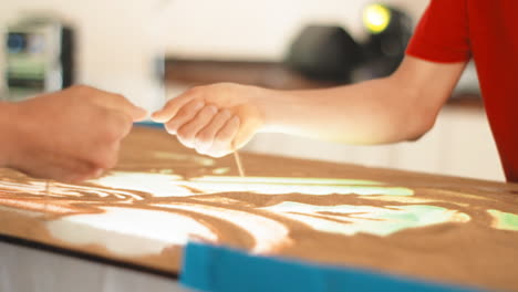 closeup-of-sand-art-painting-with-hand-working-hard