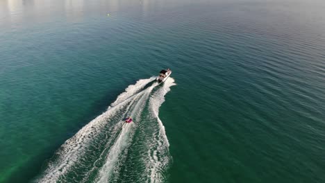 Aerial-follows-child-tubing-behind-powerboat-in-clear-green-water