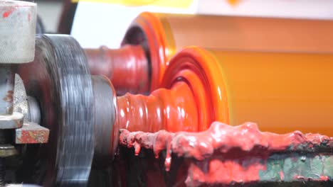 Close-Up-Of-Metal-Rollers-In-Factory-With-Orange-Paint-Fluid-Turning