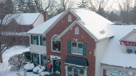 Aerial-of-front-exterior-of-house-covered-in-snow,-decorated-for-Christmas