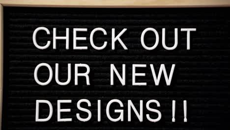 Check-out-our-new-designs-black-letter-pin-board-with-white-words-pressed-in-with-wood-frame,-camera-close-pulling-out
