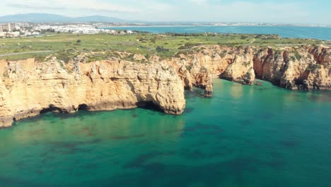 Steile-Felsvorsprünge-Und-Ruhiges-Smaragdgrünes-Wasser-In-Lagos-Algarve,-Portugal---Breite-Antennenaufnahme