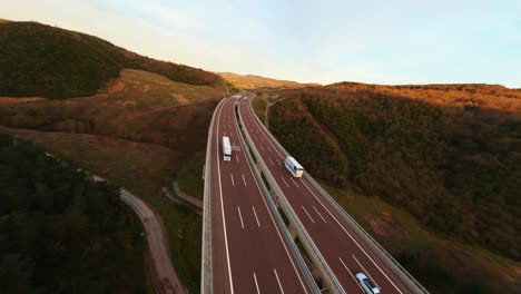 Aerial-view-of-traffic-highway-through-a-green-forest-during-sunset-at-autumn-season