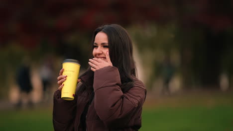 A-Lovely-Woman-Holding-A-Coffee-Laughing-At-The-Park-Of-Iulius,-Cluj-Napoca-In-Romania
