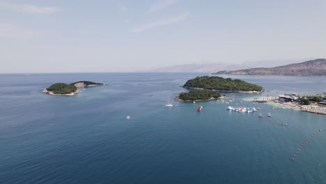 Aerial-shot-of-beach-and-islands-surrounded-by-boats-and-yachts-in-Ksamil,-Albania