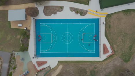 Weicher-Drohnen-Akzent,-Während-Junge-Leute-Mit-Ihren-Freunden-Auf-Einem-Blauen-Platz-Basketball-Spielen