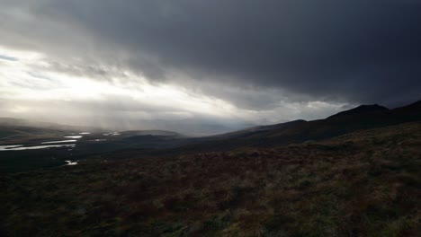 Ein-Schwenk-Zeigt-Langsam-Eine-Dunkle,-Stimmungsvolle-Landschaft-Mit-Bergen-Und-Lochs-Im-Nordwestlichen-Hochland-Von-Schottland,-Während-Lichtstrahlen-Den-Himmel-In-Der-Ferne-Durchdringen