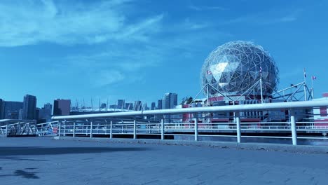 Loop-lady-jogging-back-view-along-waterfront-pier-of-Vancouver-Olympic-village-background-Science-World-modern-city-skyline-on-a-sunny-cobblestone-day-with-light-clouds-she's-blonde-wearing-gray-white