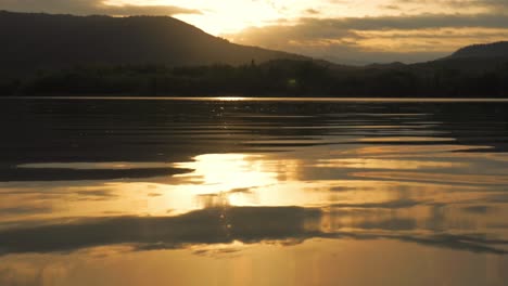 Schöner-Sonnenuntergang,-Der-Sich-Auf-Wasser-Mit-Bergen-Im-Hintergrund-Widerspiegelt