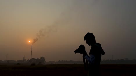 Medium-close-up-of-man-photographing-industrial-area,-hazy-sunset,-static