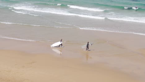 Dos-Surfistas-Cargando-Sus-Tablas-De-Surf-En-La-Playa-De-Praia-Do-Guincho,-Portugal