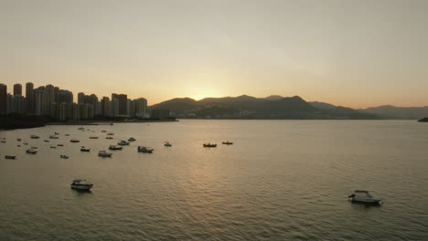 Luftstadtbild-Von-Hongkong-Während-Des-Sonnenuntergangs-Mit-Boot,-Das-In-Der-Hafenbucht-Und-Stadtbild-Im-Hintergrund-Festgemacht-Ist