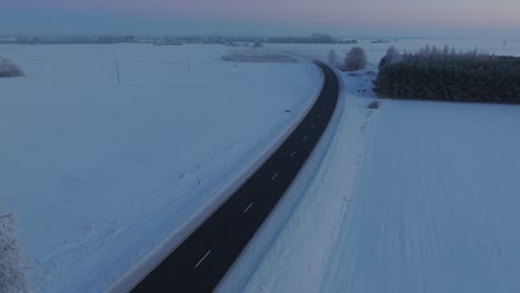 Aerial-establishing-shot-of-a-rural-landscape,-countryside-road-with-truck,-agricultural-fields-and-trees-covered-with-snow,-cold-freezing-weather,-golden-hour-light,-wide-drone-shot-moving-backward