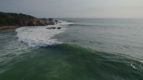 Wide-drone-shot-of-surfers-trying-to-ride-a-big-wave-off-the-coast-of-Mexico