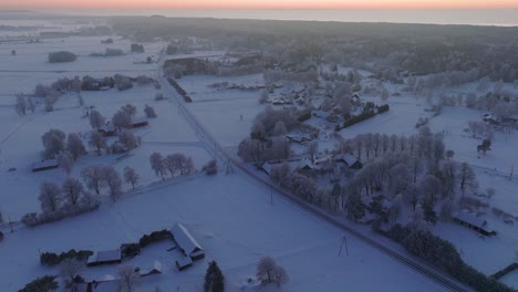Aerial-establishing-shot-of-a-rural-landscape,-countryside,-agricultural-fields-and-trees-covered-with-snow,-cold-freezing-weather,-sunset-golden-hour-light-glow,-wide-drone-shot-moving-forward-slow