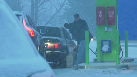 Busy-Neste-petrol-station-with-queues-of-people-refilling-their-cars-in-fear-of-fuel-shortages,-rising-prices,-hype-at-gas-stations,-overcast-winter-day-with-heavy-snowstorm,-medium-handheld-shot