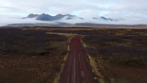 Drone-flight-over-dirt-road-in-wild-Icelandic-landscape,-view-of-misty-mountains