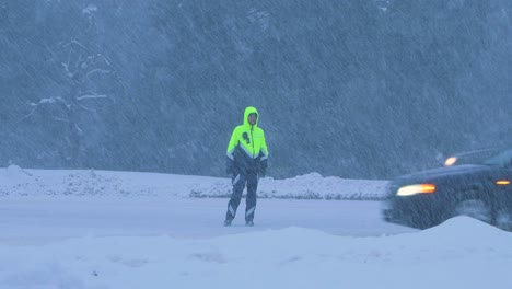 Latvian-road-police-officer-organizing-car-traffic-during-a-heavy-snow-blizzard,-overcast-winter-day,-handheld-distant-medium-shot