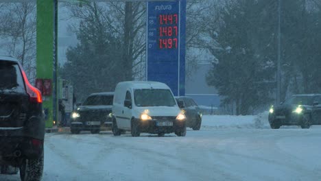 Busy-Neste-petrol-station-with-queues-of-people-refilling-their-cars-in-fear-of-fuel-shortages,-rising-prices,-hype-at-gas-stations,-overcast-winter-day-with-heavy-snowstorm,-distant-medium-shot