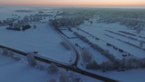 Aerial-establishing-shot-of-a-rural-landscape,-countryside-roads,-agricultural-fields-and-trees-covered-with-snow,-cold-freezing-weather,-sunset-golden-hour-light,-wide-drone-shot-moving-forward-high