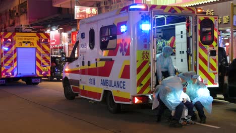 Un-Paciente-Anciano-Es-Llevado-En-Una-Camilla-A-Una-Ambulancia-Mientras-Un-Equipo-De-La-Unidad-De-Emergencia-De-Primeros-Auxilios,-Incluidos-Bomberos-Y-Un-Equipo-Médico,-Responde-A-Una-Llamada-De-Socorro-En-Hong-Kong
