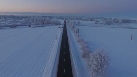 Aerial-establishing-shot-of-a-rural-landscape-with-road-and-cars,-countryside,-agricultural-fields-and-trees-covered-with-snow,-cold-freezing-weather,-golden-hour-light,-wide-drone-shot-moving-forward