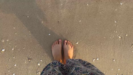 Slim-female-legs-and-feet-stand-along-sea-water-waves-on-sandy-beach-in-Doha-Qatar
