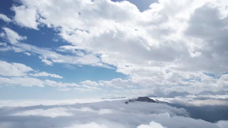High-altitude-aerial-drone-view,-flying-above-fluffy-clouds-and-Mountains