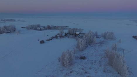 Aerial-establishing-shot-of-a-rural-landscape,-countryside-house,-agricultural-fields-and-trees-covered-with-snow,-cold-freezing-weather,-sunset-golden-hour-light,-wide-drone-shot-moving-forward-slow