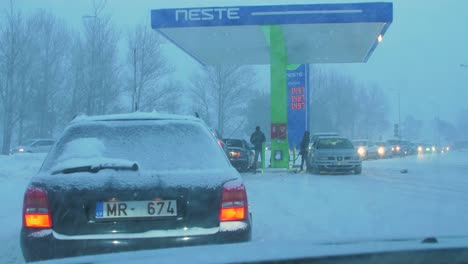 Busy-Neste-petrol-station-with-queues-of-people-refilling-their-cars-in-fear-of-fuel-shortages,-rising-prices,-hype-at-gas-stations,-overcast-winter-day-with-heavy-snowstorm,-wide-handheld-shot