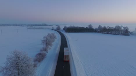Aerial-establishing-shot-of-a-rural-landscape,-countryside-road-with-cars,-agricultural-fields-and-trees-covered-with-snow,-cold-freezing-weather,-golden-hour-light,-wide-drone-shot-moving-forward