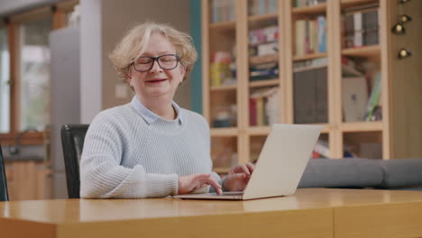 Elderly-caucasian-woman-uses-laptop-and-looks-up-with-content-smile