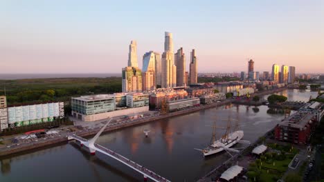 Aerial-view-dolly-in-of-the-Puente-de-la-Mujer-with-the-luxury-skyscrapers-of-Puerto-Madero-at-sunset,-Buenos-Aires,-Argentina