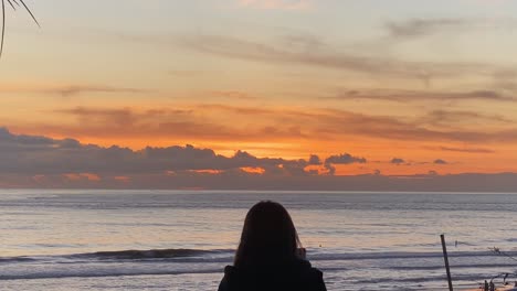 Touristin-Am-Strand-Von-Carcavelos-Fotografiert-Kleine-Wellen,-Die-An-Sonnigen-Tagen-Vor-Einem-Riesigen-Sonnenuntergang-über-Dem-Meer-Stehen
