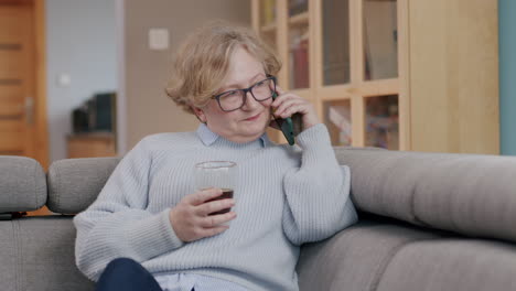 Elderly-caucasian-woman-at-home-speaks-on-phone-with-drink-in-hand