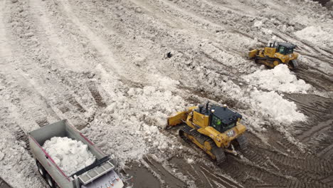 Yellow-crawler-tractor-bulldozer-with-a-bucket-works-in-winter-clearing-the-snow-dump-site