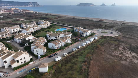 Aerial-view-orbiting-row-of-campervans-parked-on-Estartit-beach-resort-coastline-over-looking-Medes-islands-skyline