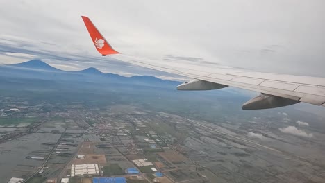 Lion-Air-plane-flying-above-rural-town-on-Indonesia,-window-view