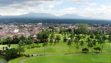 Palm-trees,-Indonesian-city-and-mountain-range-in-horizon,-aerial-view
