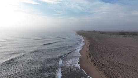 Empty-misty-sunrise-beach-and-shimmering-rippled-ocean-coastline-aerial-view