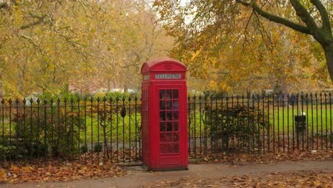 Classic-Red-Telephone-Booth-In-City-Park-During-Autumn-Season-In-London,-UK