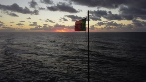 Static-shot-of-Portuguese-flag-in-the-wind,-Strong-wind-moving-flag-by-the-Atlantic-Ocean-during-Sunset