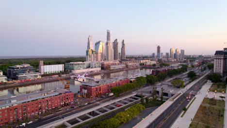 Dolly-in-aerial-view-of-the-docks-of-Puerto-Madero-with-luxury-restaurants-and-the-Puente-de-la-Mujer,-exclusive-skyscrapers-in-the-background,-epic-sunset
