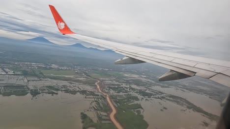 Plane-with-Lion-Group-logo-flying-above-flooded-lands-of-Indonesia,-window-view