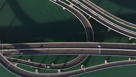 Bird's-eye-view-aerial-drone-rising-shot-of-traffic-on-intertwined-bridge-network-over-water