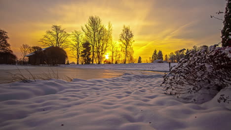 Timelapse-shot-of-wooden-cottage-surrounded-by-white-snow-with-frozen-lake-in-the-foreground-at-sunrise
