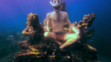 Junger-Mann-Mit-Maske-Und-Schnorchel-Meditiert-Unter-Dem-Meer-Neben-Einigen-Untergetauchten-Asiatischen-Statuen