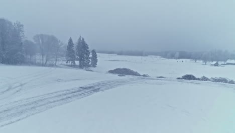 Aerial-drone-shot-over-icy-road-and-farmlands-covered-with-snow-while-heavy-snowing-on-a-foggy-winter-day